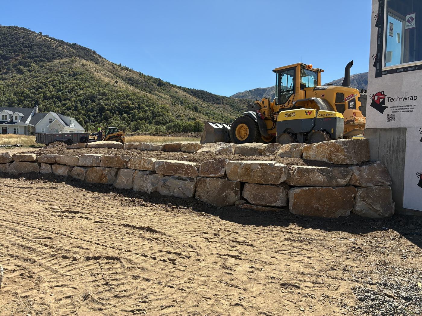 A long boulder retaining wall with the loader and roller behind it