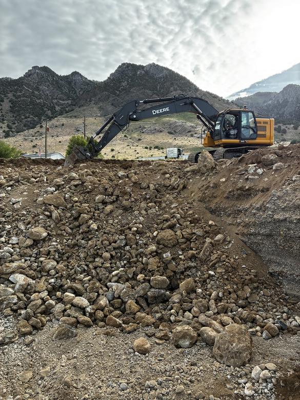 An excavator working the top of a large rock spoil pile