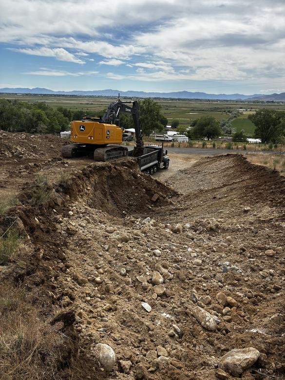 An excavator loading a dump truck on a hillside cut