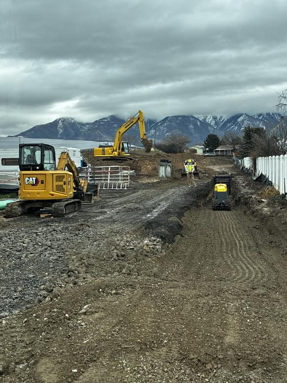 Two excavators and the crew grading a roadway over a compacted trench