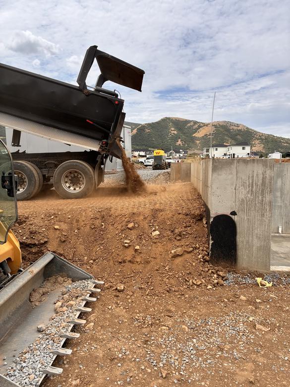A dump truck backfilling against a finished foundation wall