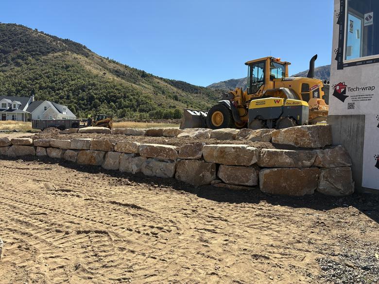 A long boulder retaining wall with the loader and roller behind it