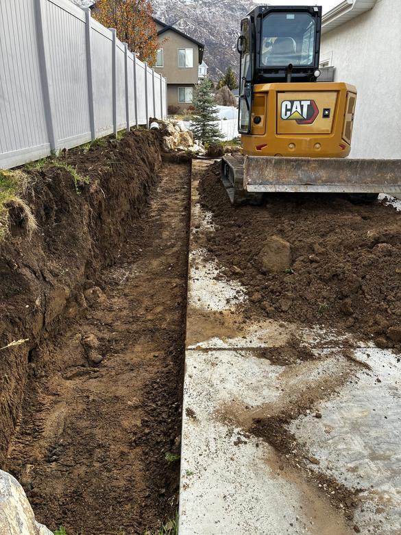 A footing trench dug along a fence line for a new wall