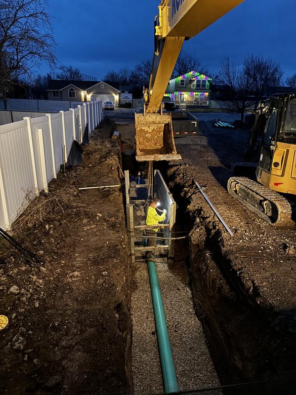 A deep sewer trench worked behind a trench shield at dusk