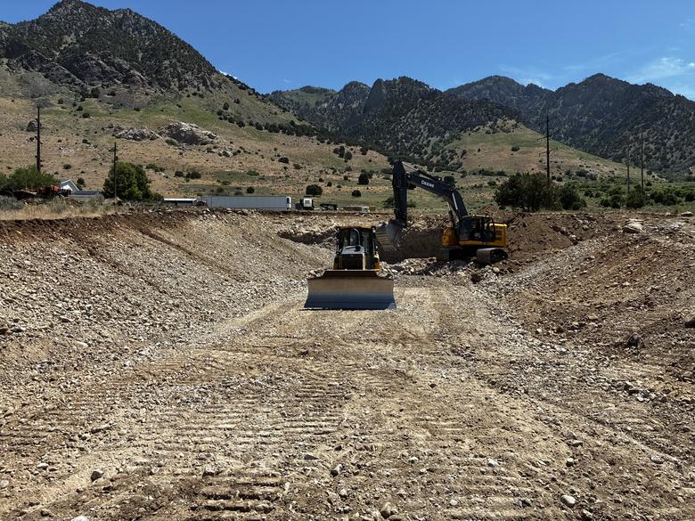 A dozer and an excavator moving dirt across a wide excavated basin