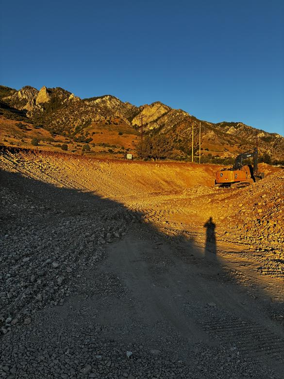 An excavator on a freshly graded cut slope at sunset