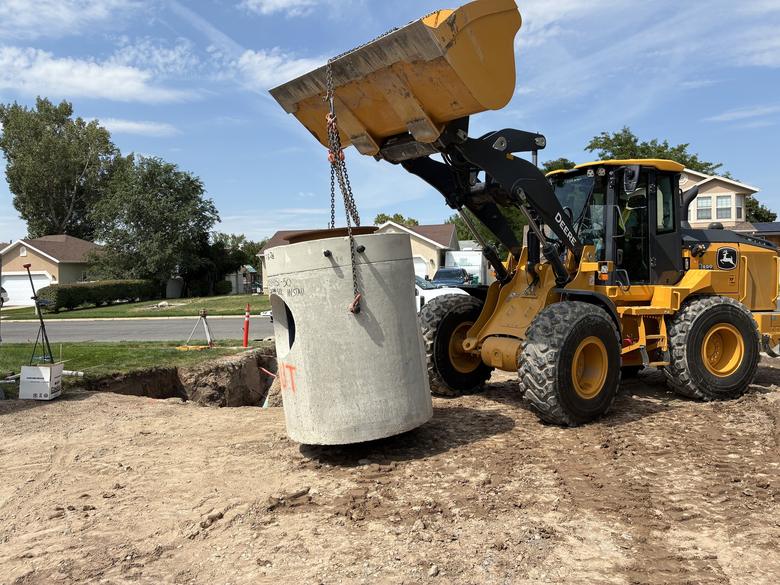 A loader carrying a concrete manhole barrel across the site
